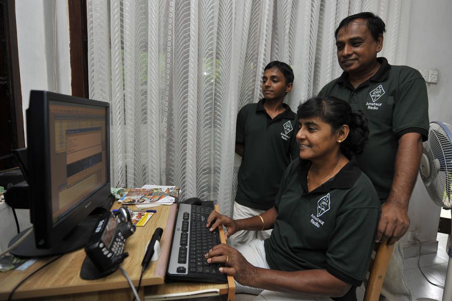 Sri Lanka Sitting: Rajini, 4S6ARW, makes a digital QSO on the 10-meter band, while Senarath, 4S6WAS, stands behind her. Their son, Reshan, 4S6YRW, is supervising his mother in action.